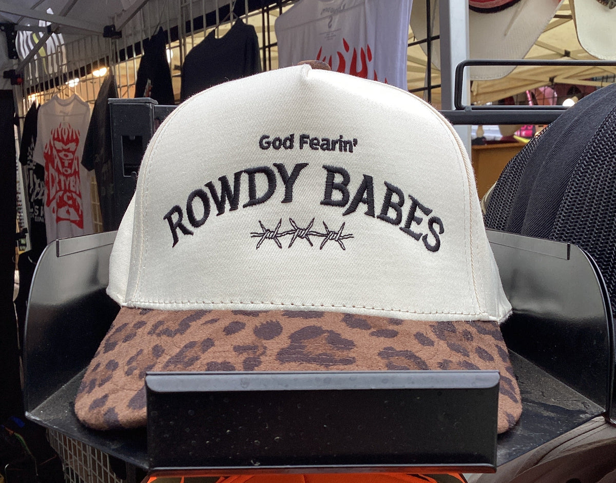 A white snapback cap with a leopard-print visor, featuring the text 'God Fearin' ROWDY BABES' embroidered on the front. The hat is displayed on a black stand in a retail store setting.